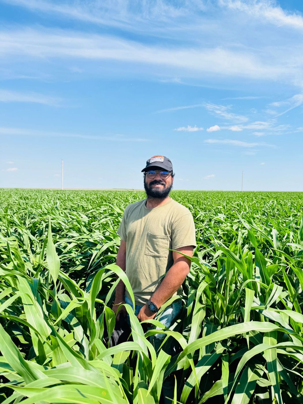 Abinava Yeshwanth KJ standing in a green crop field under a blue sky