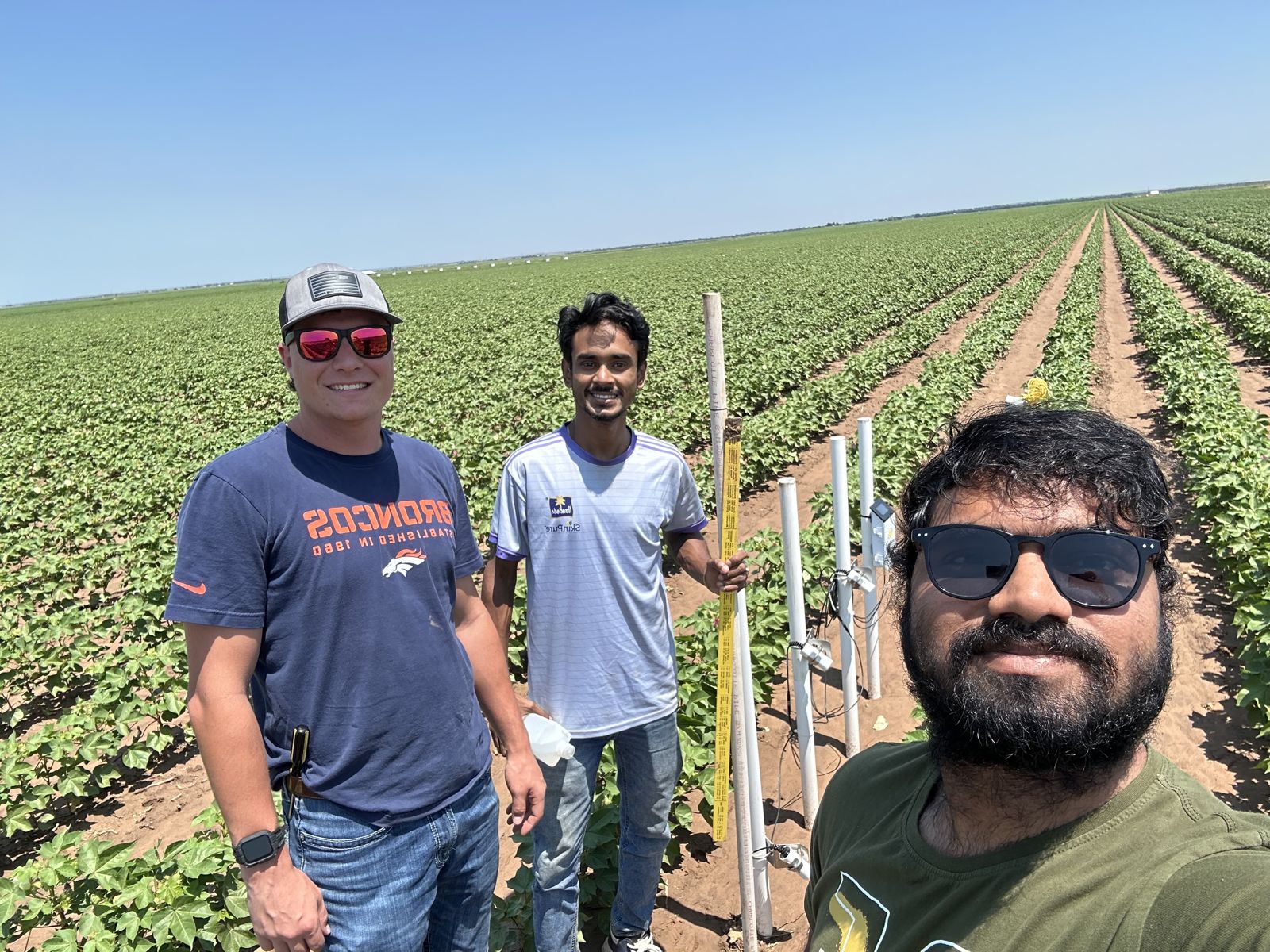 Abinava Yeshwanth KJ with two colleagues beside a field sensor station in a cotton field
